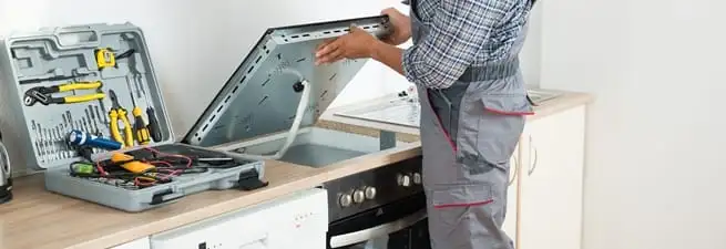 Cooktop repair technician lifting a built-in stovetop for service in Yonkers, NY