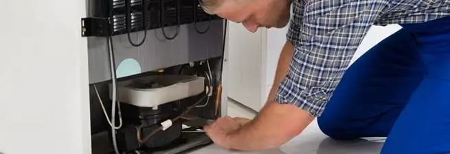 Refrigerator repair technician servicing the compressor and condenser area in Yonkers, NY