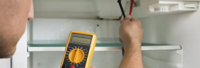 Refrigerator repair technician testing electrical components with a multimeter in Yonkers, NY